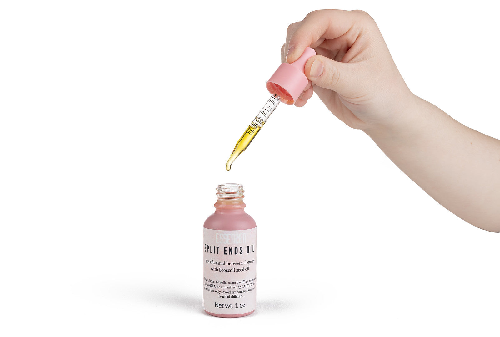 Hand using a dropper to add liquid from a pink bottle labeled 'Split Ends Milk' on a white background